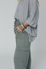 Side view of the Easy Mornings Cinched Pants by Three Bird Nest in light olive, styled with a loose gray top and bracelets.