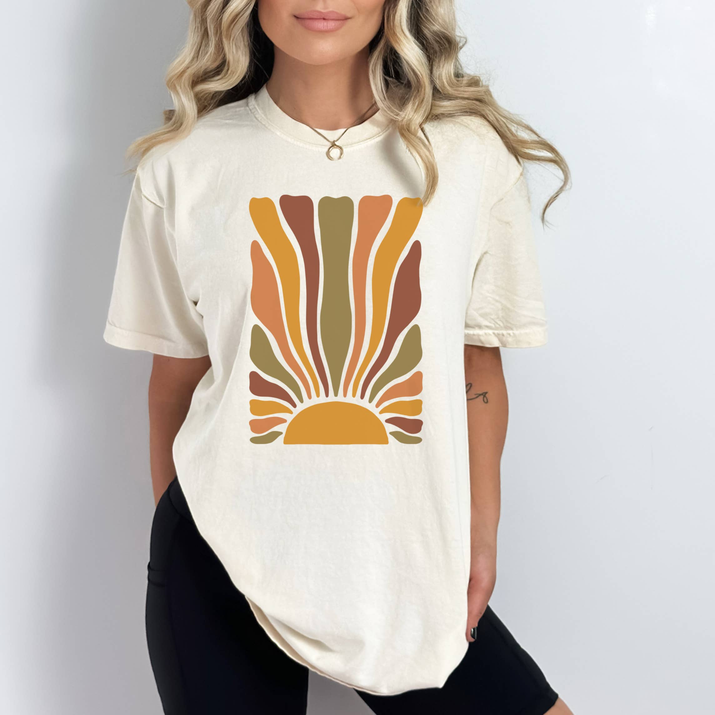 A person wearing a beige t-shirt with a retro sun design printed on the front, paired with black pants.