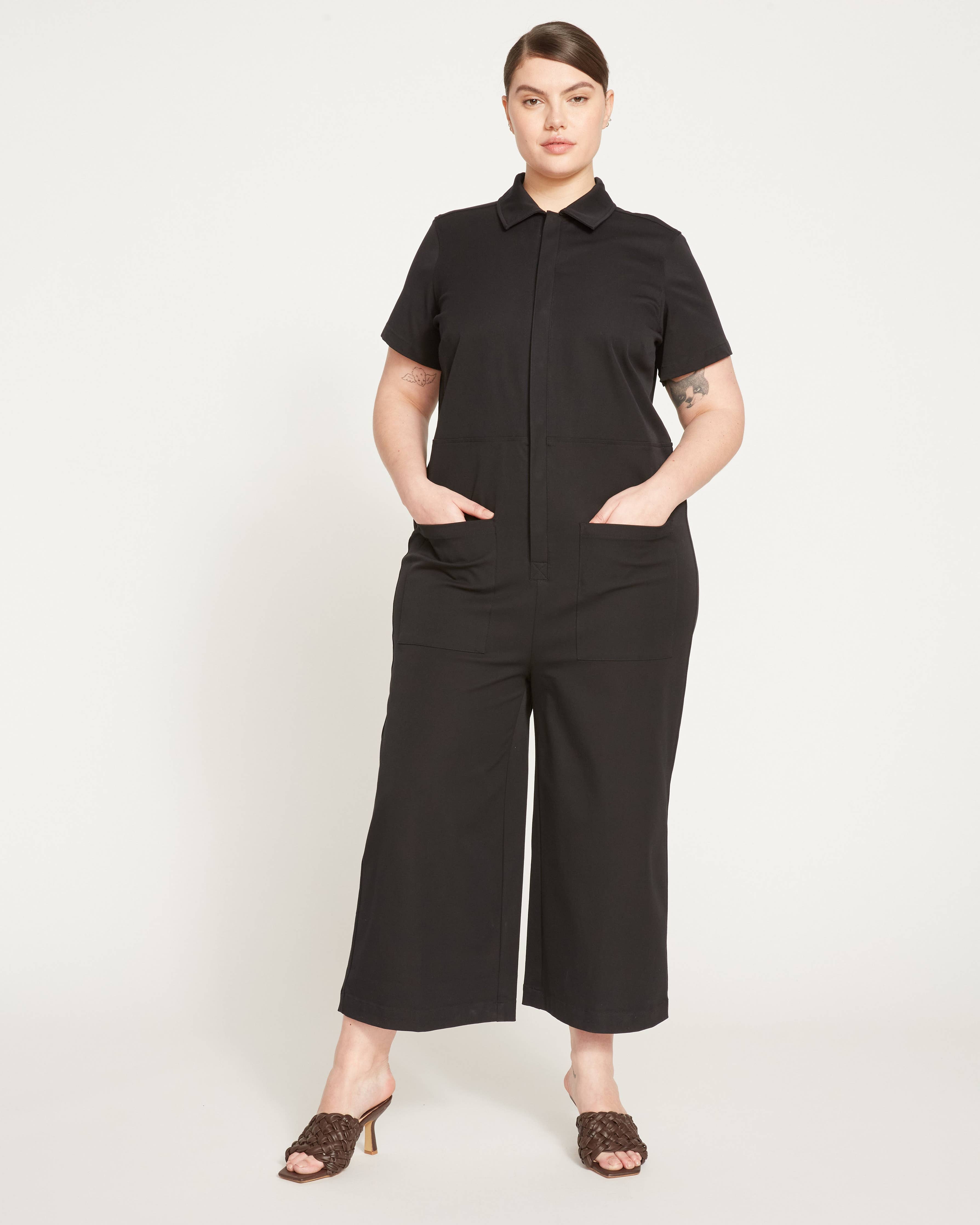 Front full-body view of the Kate Stretch Jumpsuit in black, styled with heeled mules for an elevated look.