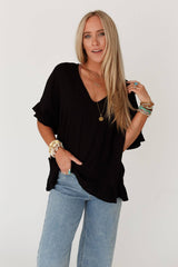 Model wearing the THREE BIRD Nest Let Me Be Ruffled Top in black, styled with layered boho jewelry and denim for a carefree, sun-ready look.