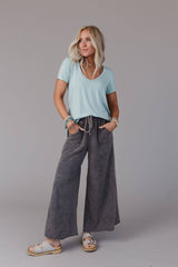 Styled view of the Three Bird Nest Scoop Neck Bralette Tee in washed seafoam, paired with grey wide-leg pants and layered bracelets.
META Description: