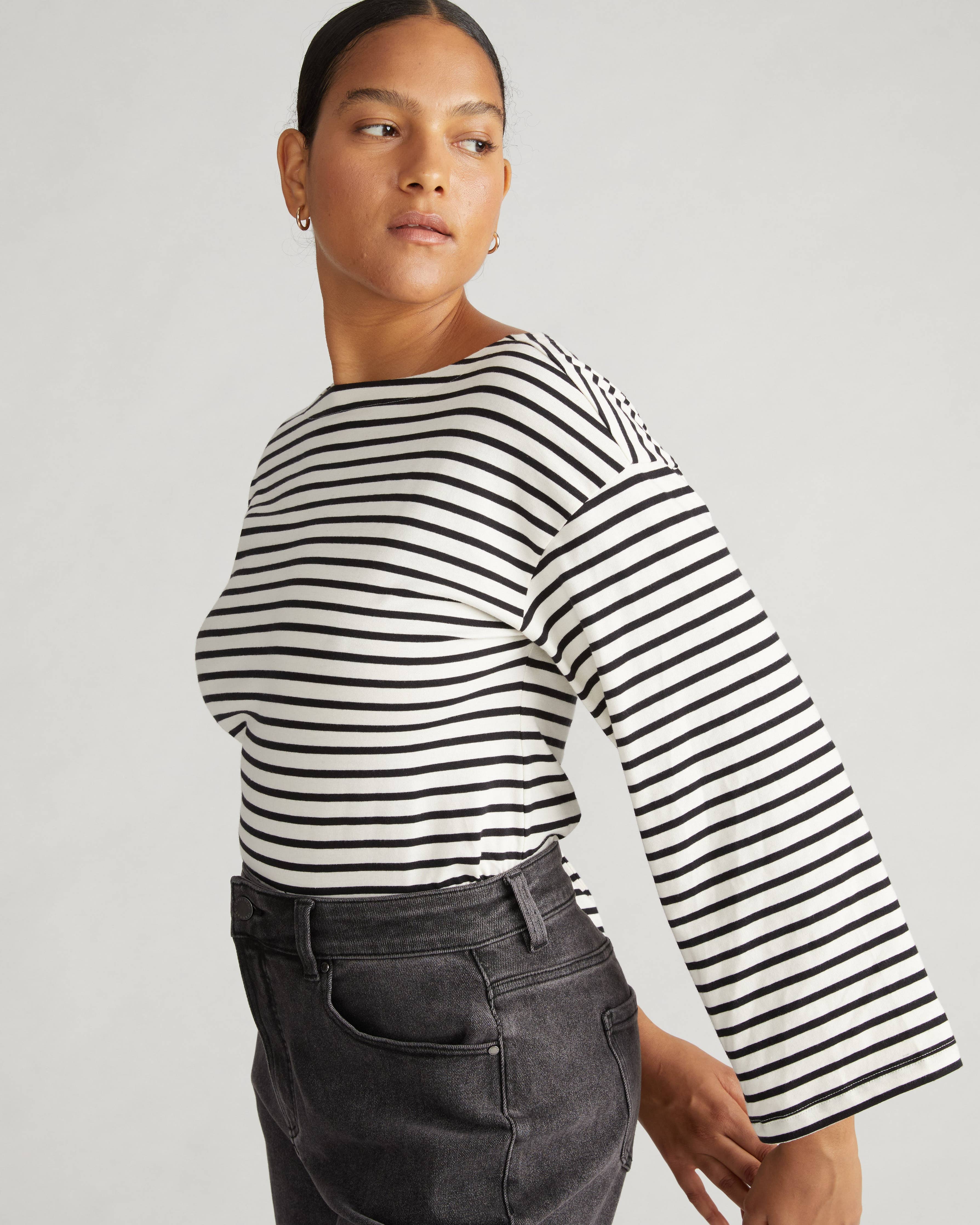 Side view of the Universal Standard Montauk Breton Stripe Bell Sleeve Top in ecru and black stripe, showcasing the bell sleeves and boat neckline.
