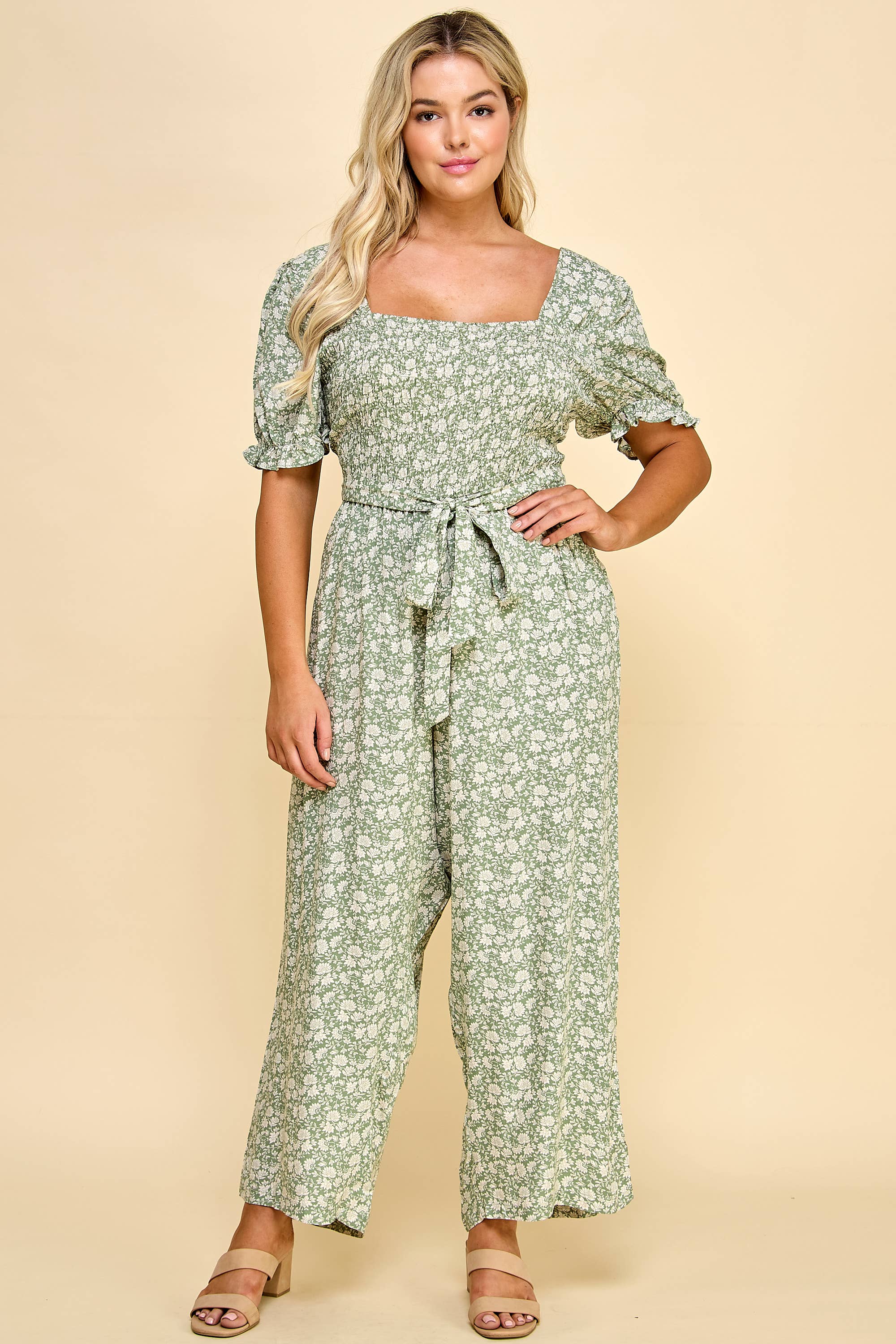 Front view of the Winslow Collection gaucho jumpsuit in plus size, featuring a green floral print, puff sleeves, and a waist tie for a flattering fit.